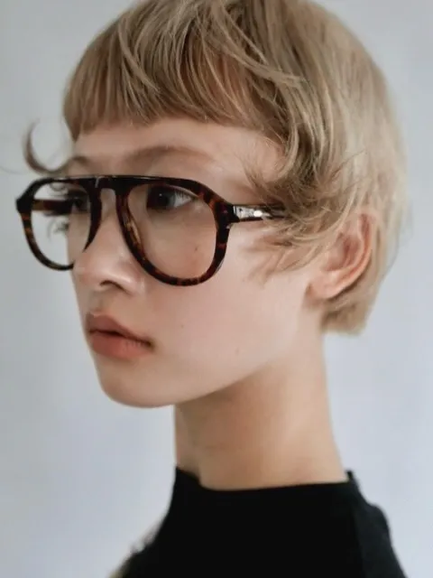 Cropped blonde pixie with baby bangs and oversized dark glasses