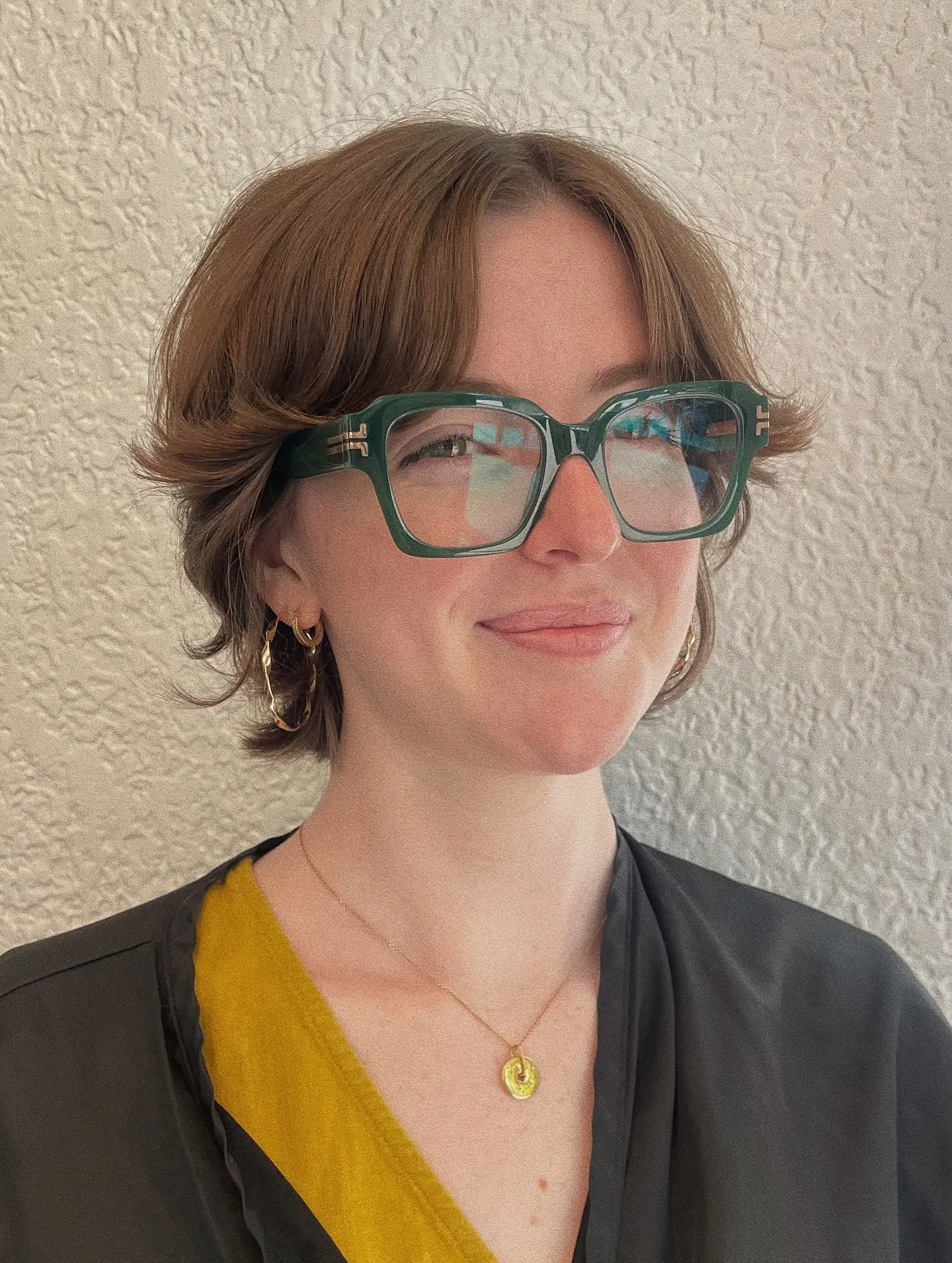 Short layered crop with centre-parted fringe, flipped ends, and green glasses