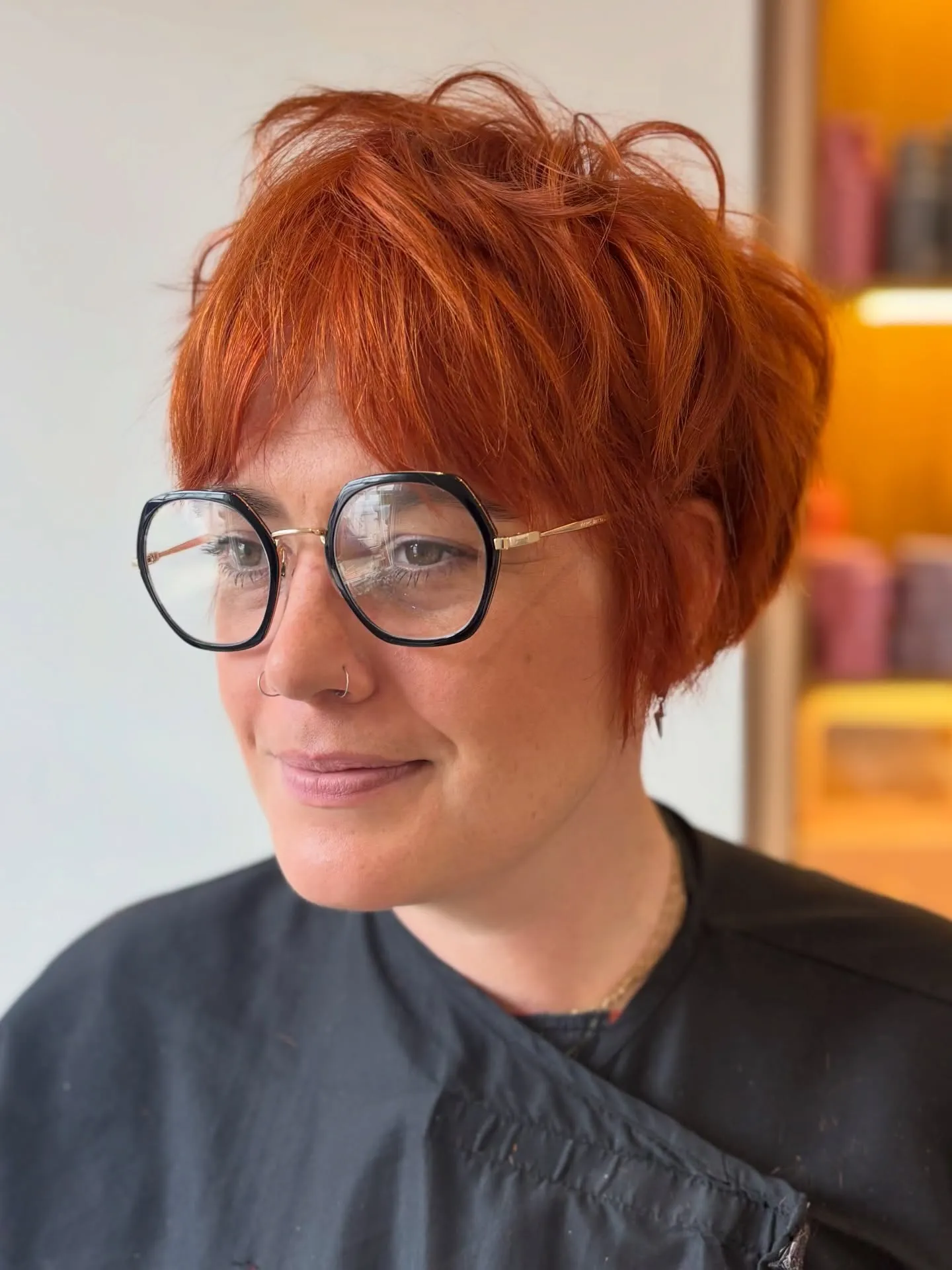 Textured copper pixie cut with long fringe and round black glasses