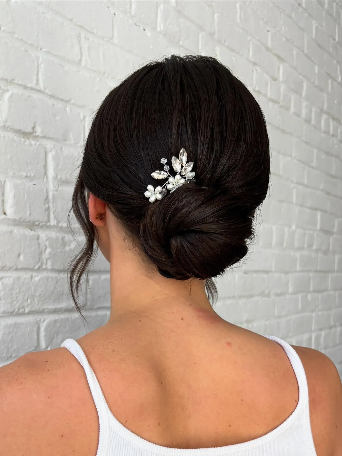 Dark smooth bridal low bun with a small crystal floral hair pin