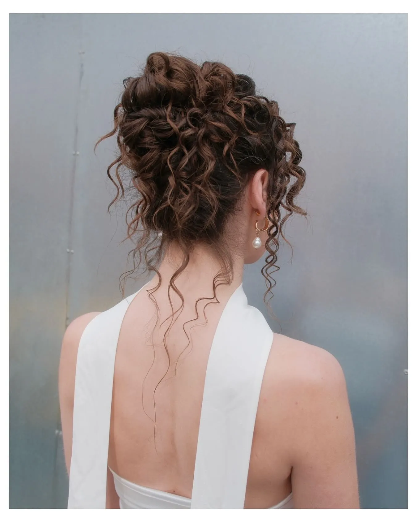 Curly brunette bridal updo with loose tendrils and high volume