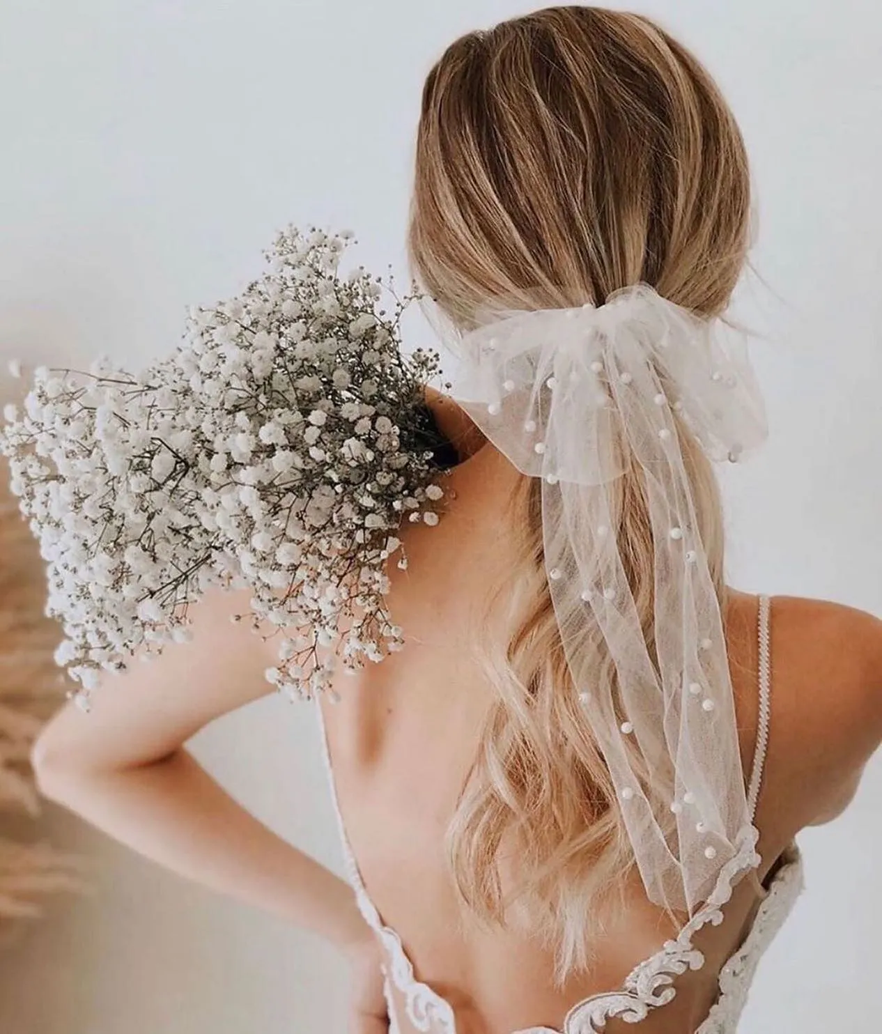 Simple blonde bridal low ponytail with a soft dotted veil bow