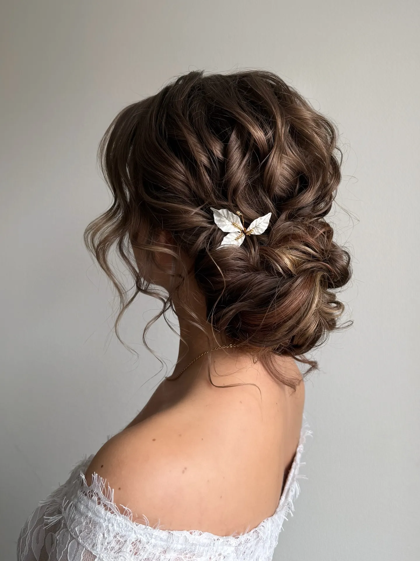 Curly brunette bridal updo with loose ringlets and a leaf hair accessory