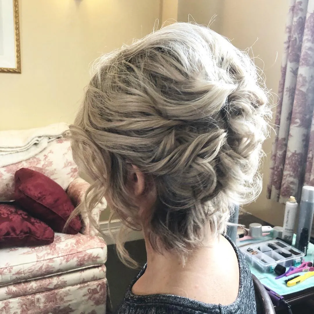Tousled curly updo for short blonde hair with loose tendrils