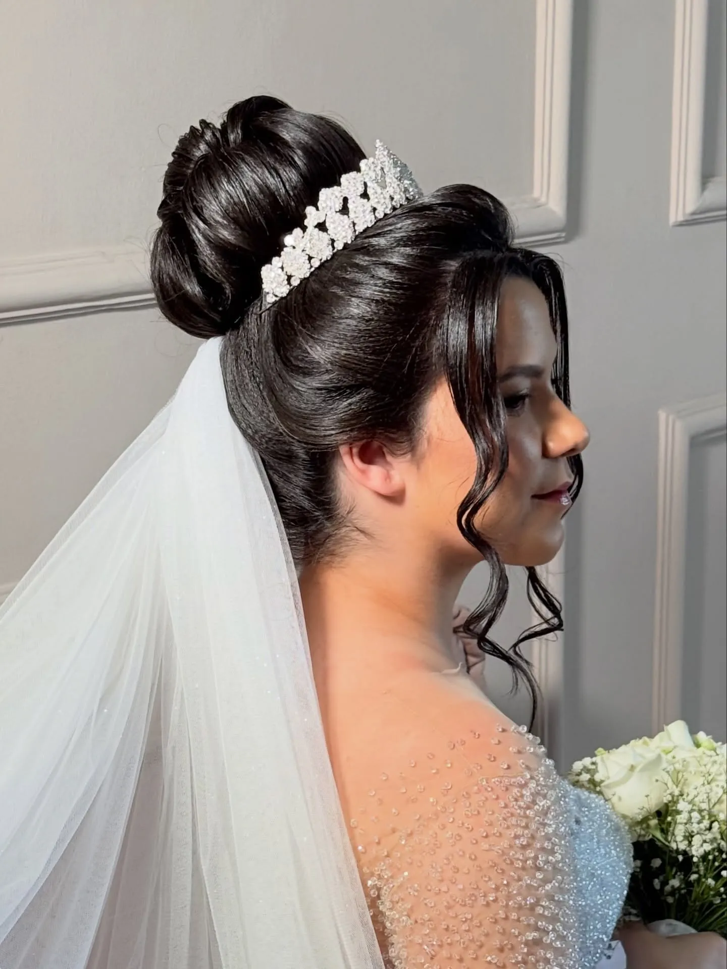 High sleek bridal bun with a pointed silver tiara and veil
