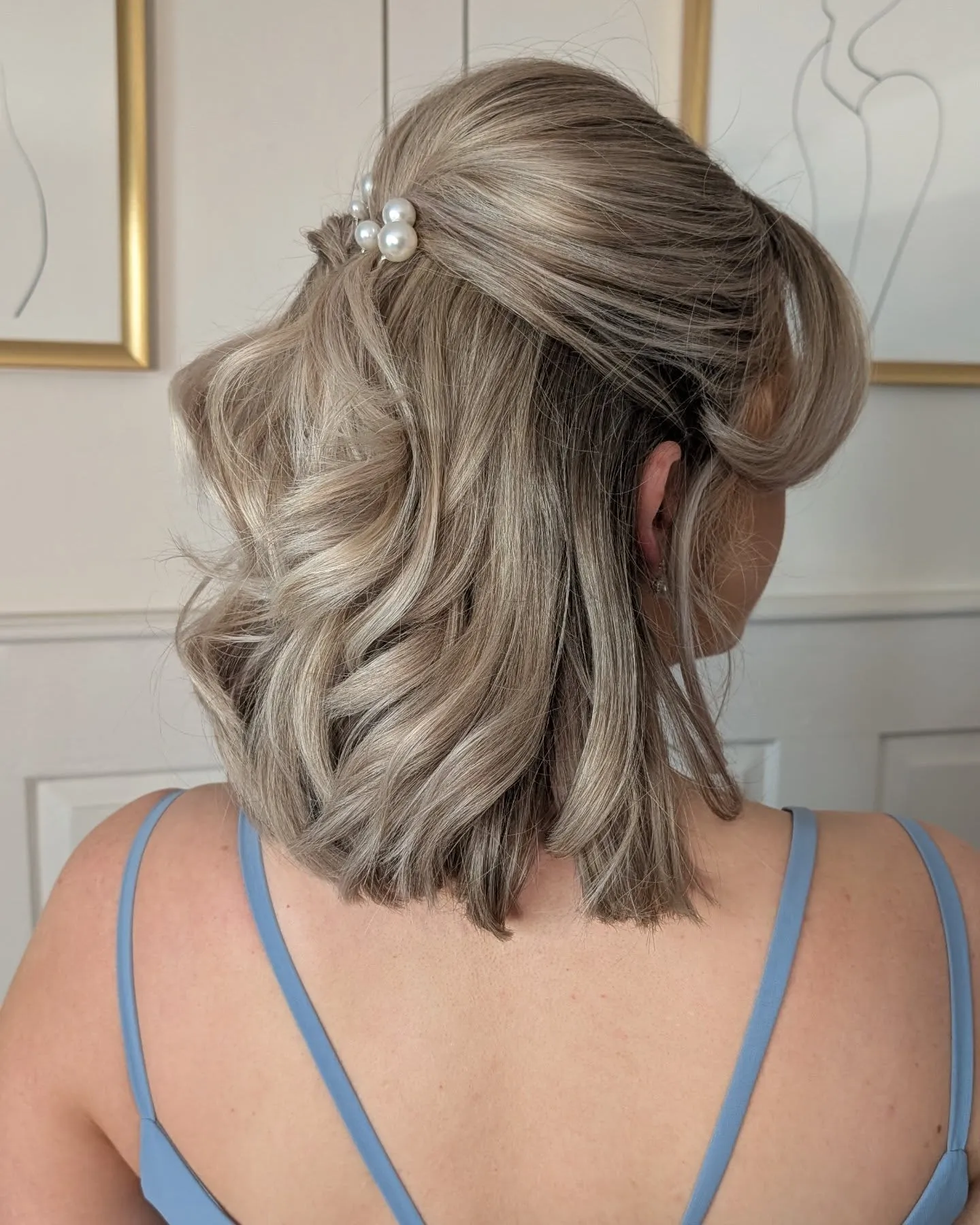 Half-up blonde shoulder-length waves secured with a pearl clip