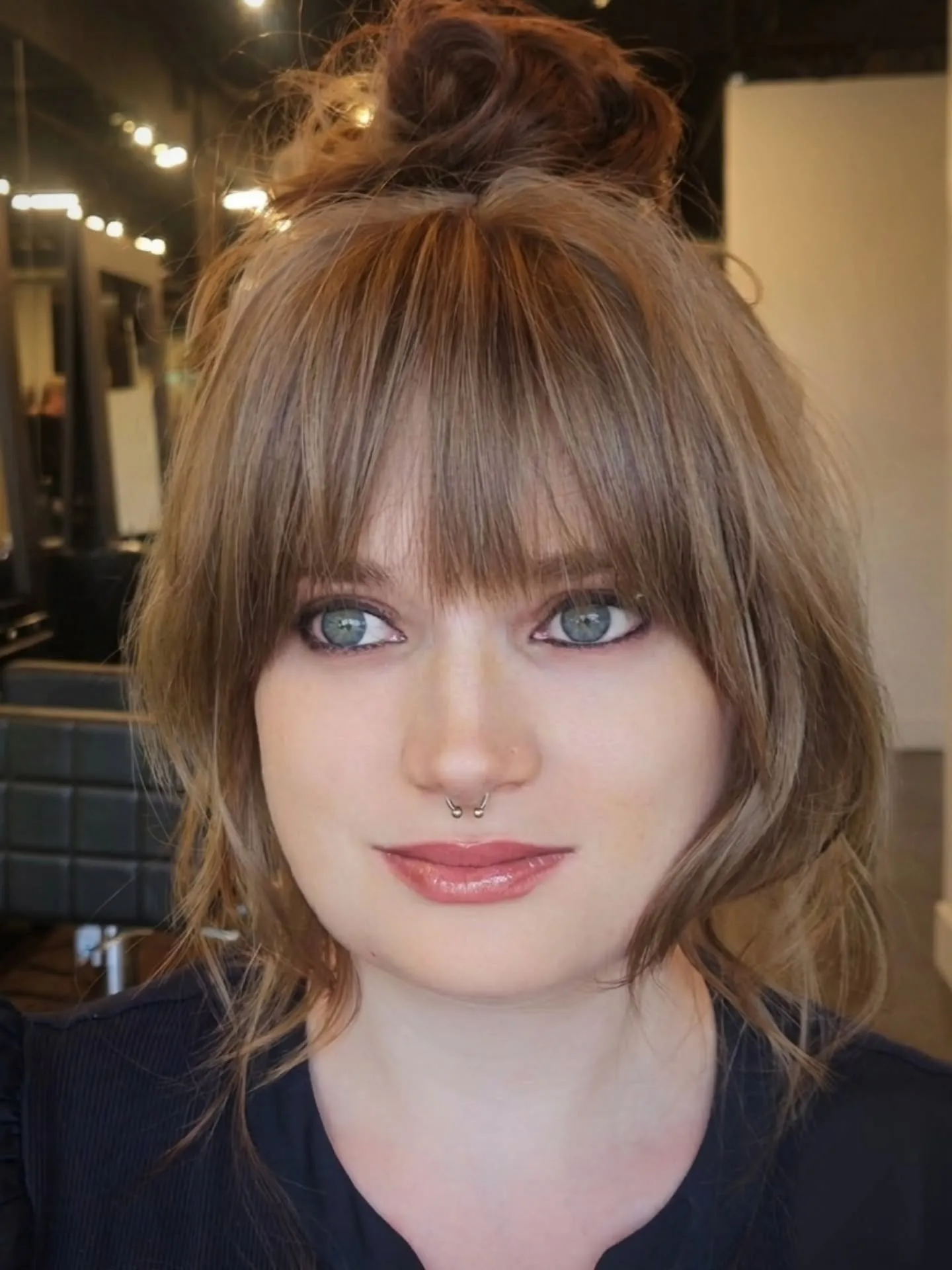 Messy high bun with a straight full fringe and loose face-framing strands