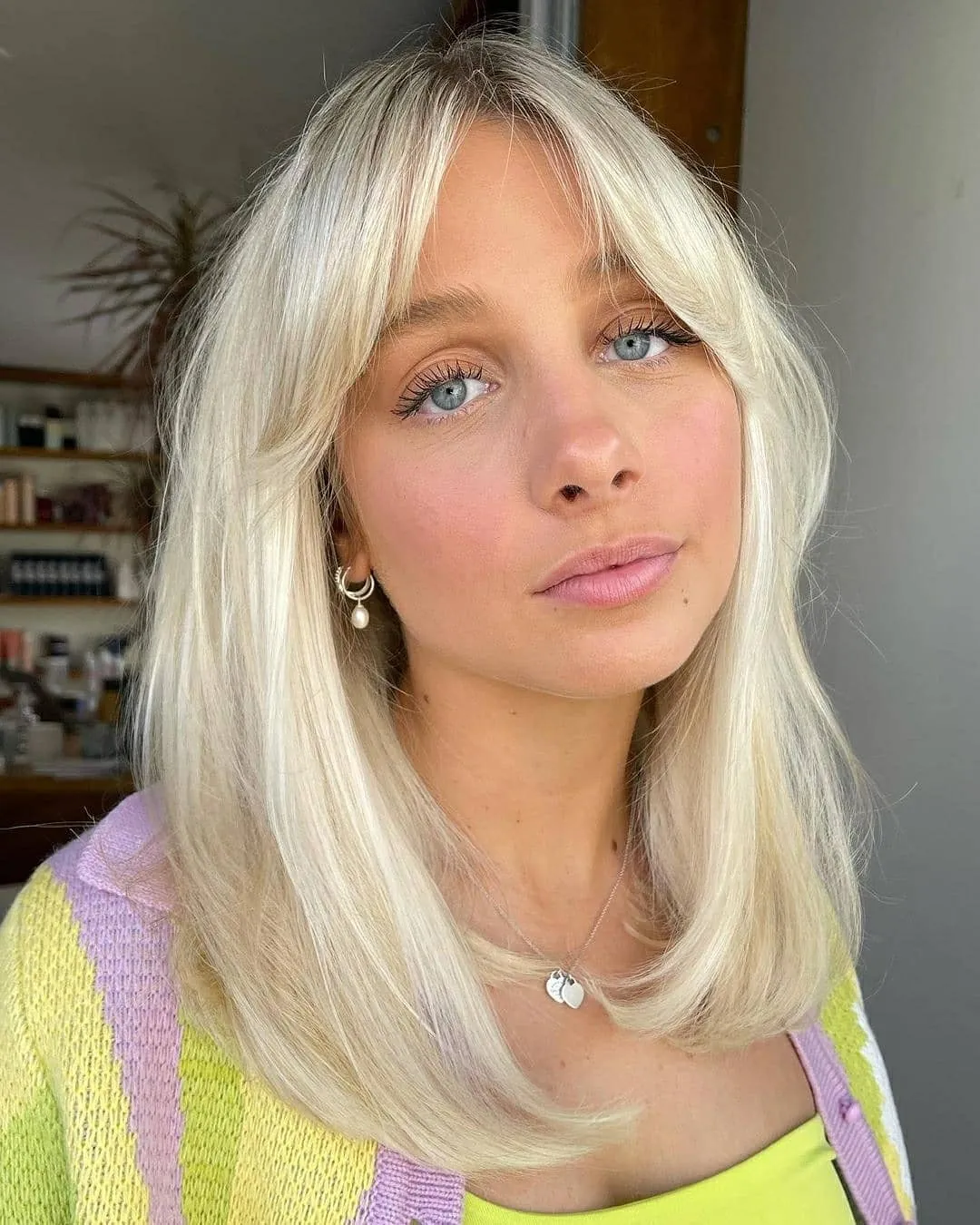 Shoulder-length blonde hair with curtain bangs and softly curved ends