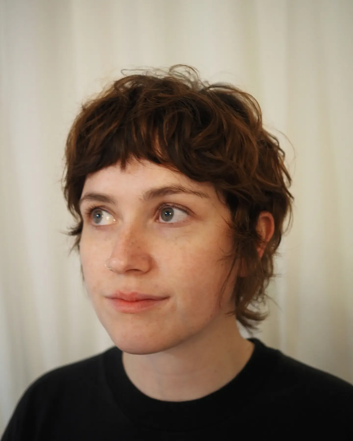 Brown shaggy pixie with micro bangs and longer nape curls