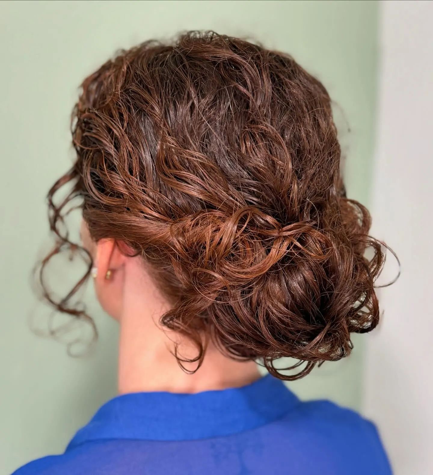Low curly bun with twisted sides and loose tendrils